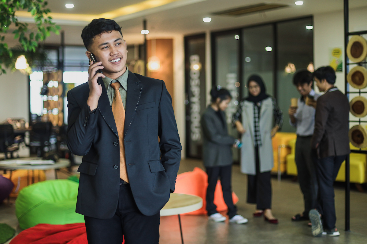 Young business professional talking on the phone with his colleagues in the background